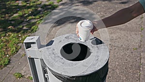 A woman's hand tosses a to-go coffee cup into a trash bin, let's halt planet pollution.