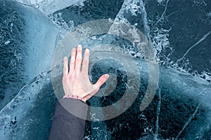 Woman`s hand touches the clear blue cracked ice of Lake Baikal. Top view