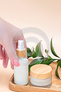 Woman& x27;s hand touches a mockup of white bottle of cream. Unlabeled packaging for cosmetics in sunlight on beige