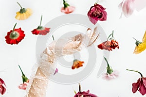 A woman\'s hand in a transparent glove touches floating flowers in a light spring studio. Beauty and fashion