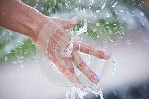 A woman's hand under splashes of water from a fountain