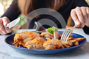 A woman`s hand using knife and fork to eat fried chicken and french fries in restaurant