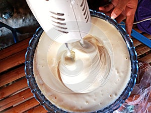 A woman& x27;s hand using mixer kitchen tool to mix egg mixture for making tart cakes