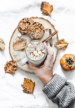 Woman`s hand in a warm sweater holds cup of hot chocolate. Cookies with chocolate chips and mug of hot chocolate on a light