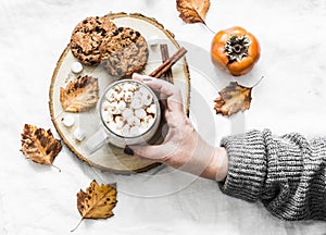 Woman`s hand in a warm sweater holds cup of hot chocolate. Cookies with chocolate chips and mug of hot chocolate on a light