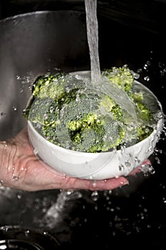 Woman`s hand washing broccoli under running water at the kitchen sink.