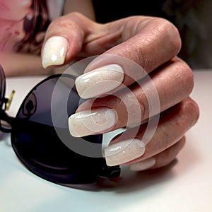 A woman& x27;s hand with a white manicure holds sunglasses