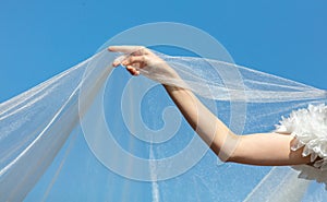 A woman& x27;s hand with a white wedding veil against a blue sky