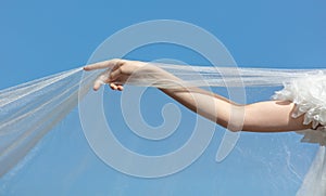 A woman& x27;s hand with a white wedding veil against a blue sky