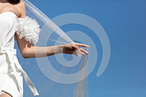 A woman's hand with a white wedding veil against a blue sky