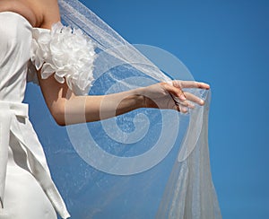 A woman& x27;s hand with a white wedding veil against a blue sky