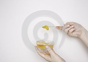 A woman`s hand with a wooden spatula and sugar paste for depilation and a jar. Light background, copyspace.