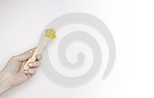 A woman`s hand with a wooden spatula and sugar paste for depilation. Light background, free space for text