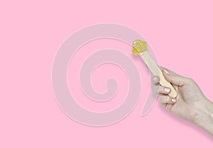 A woman`s hand with a wooden spatula and sugar paste for depilation. Pink background, copyspace