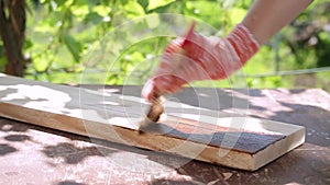 A woman's hand in a work glove paints the board with a protective impregnation