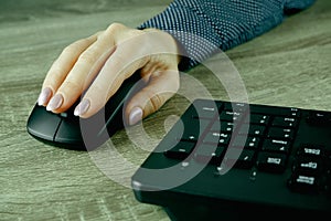 A woman\'s hand works with a mouse and keyboard manipulator. Caucasian Woman using a black wireless computer mouse on wooden