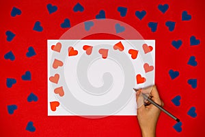 Woman`s hand write on card with red heart above red background