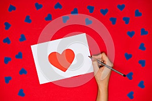 Woman`s hand write on card with red heart above red background