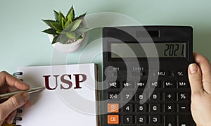 A woman`s hand writes in a notebook the acronym USP on the background of a calculator