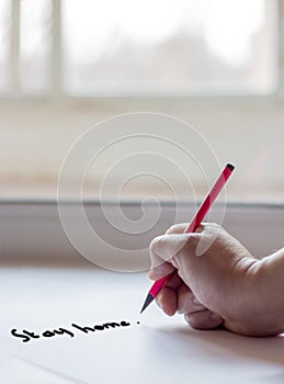 A woman`s hand writes stay at home in quarantine against the background of a spring Sunny day outside the window