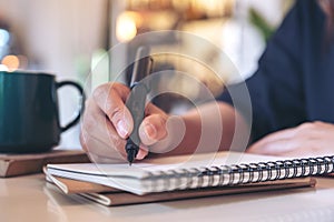 A woman`s hand writing on blank notebook with coffee cup on table in cafe