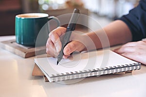 A woman`s hand writing on blank notebook with coffee cup on table in cafe
