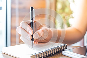 Woman`s hand is writing on a blank notepad with a pen on a woode