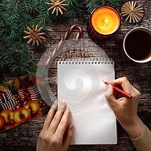 Woman's hand writing on a blank notepad sheet in Christmas setting