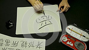 Woman`s hand writing chinese calligraphy. Female hand holding a writing brush Chinese characters