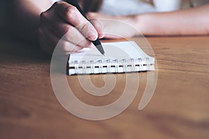 A woman`s hand writing down on a white blank notebook on wooden table