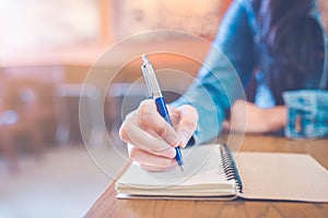 A woman`s hand is writing in empty spiral notepad with a pen.