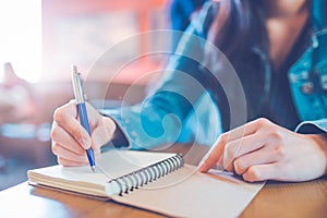 A woman`s hand is writing in empty spiral notepad with a pen.