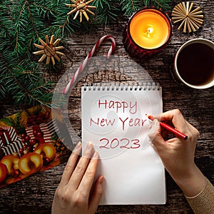 Woman's hand writing new year wishes on a notepad sheet in holiday setting
