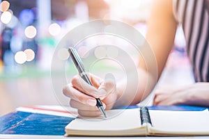 Woman`s hand writing on a notebook with a pen on a wooden desk.