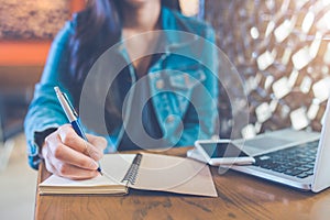 A woman`s hand is writing on a notepad with a pen and a phone wi