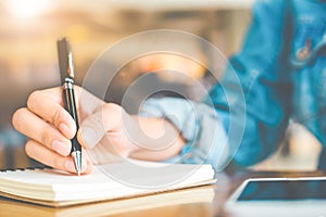 Woman`s hand writing on a notepad with a pen on a wooden desk.