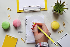 Woman's hand writing in notepad or sketchbook. Creative colorful artistic workplace. Table desk with notepads, pencil