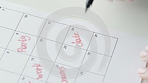 Woman`s hand writing with red felt pen on calendar word date