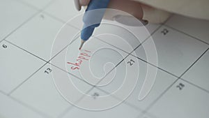 Woman`s hand writing with red felt pen on calendar word SHOPPING