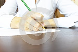 Woman`s hand writing something on paper close up. Unrecognizable business woman in white shirt writing with a pencil