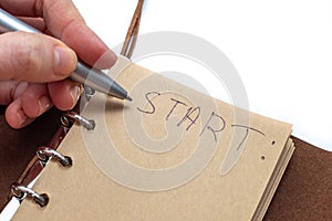 A woman`s hand wrote with a pen in a notebook: Start. the concept of starting a new, achieving goals