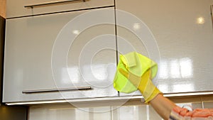 Woman`s hand in a yellow rubber glove cleans the shiny surface of a modern plastic kitchen Cabinet with a cloth. The concept of sp