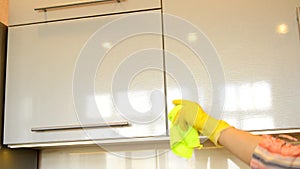 Woman`s hand in a yellow rubber glove cleans the shiny surface of a modern plastic kitchen Cabinet with a cloth. The concept of sp