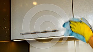 Woman`s hand in a yellow rubber glove cleans the surface of a modern plastic kitchen Cabinet with detergent and a cloth. The conce