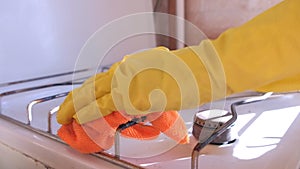 Woman`s hand in yellow rubber gloves washes dirty gas stove in kitchen.