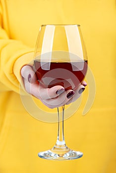 A woman's hand in a yellow sweater holds a glass of red wine.