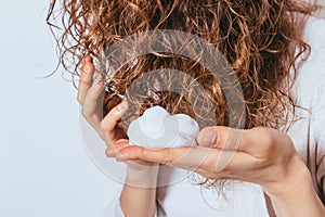 Woman's hands apply styling mousse to her curly hair photo