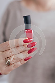 Woman`s hands and a bottle of red orange nail polish