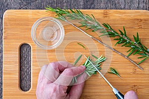 WomanÃ¢â¬â¢s hands chopping fresh sprig of rosemary with a paring knife on a bamboo cutting board, small glass bowl