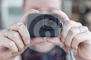 Woman`s hands close up holding a small black action camera taking a video or photo